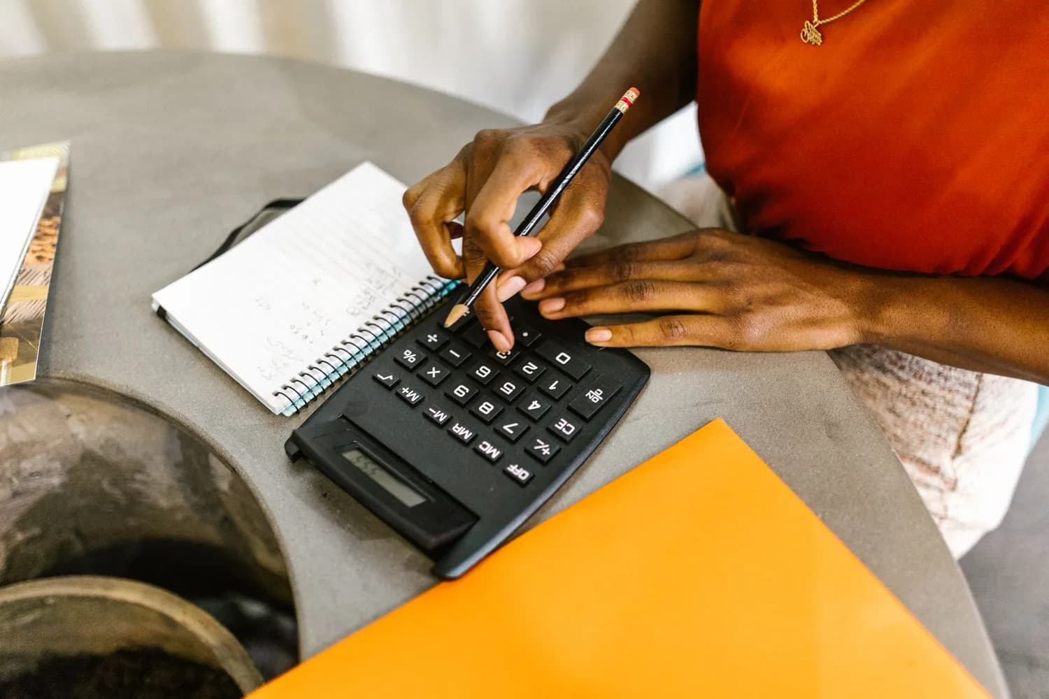 Manos usando una calculadora junto a un cuaderno y carpetas de contabilidad.